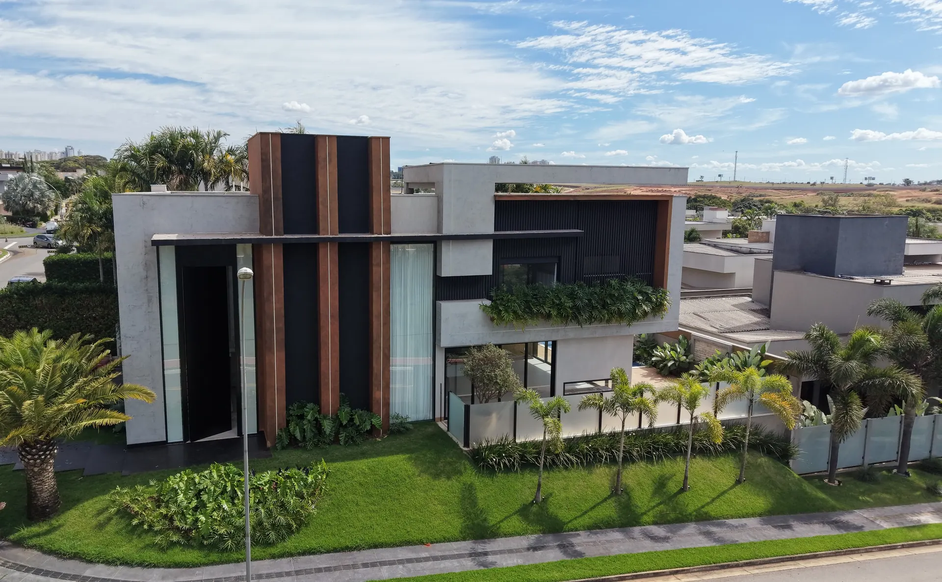 Fachada da Casa Jardins Valência vista de cima: brises verticais em tom corten, painéis ripados escuros e grandes panos de vidro com esquadrias de alumínio preto
