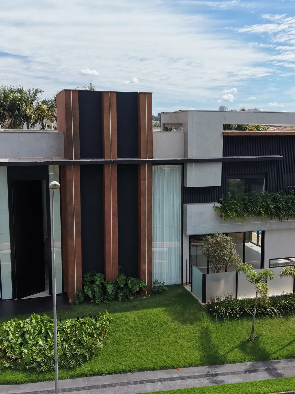 Fachada de residência de alto padrão com brises verticais em tom corten, painéis ripados escuros e esquadrias de alumínio preto