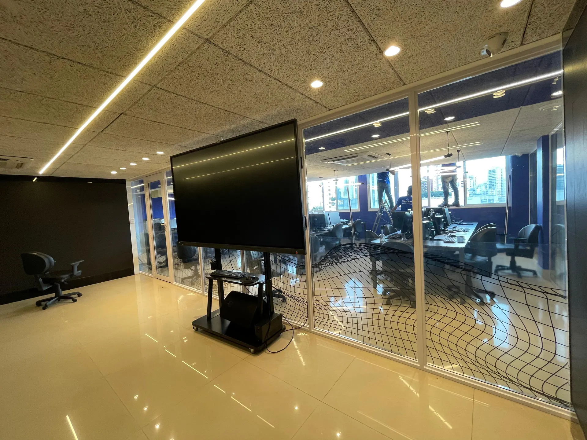 Escritório corporativo dividido por divisórias acústicas de vidro, com estações de trabalho e vista para a cidade